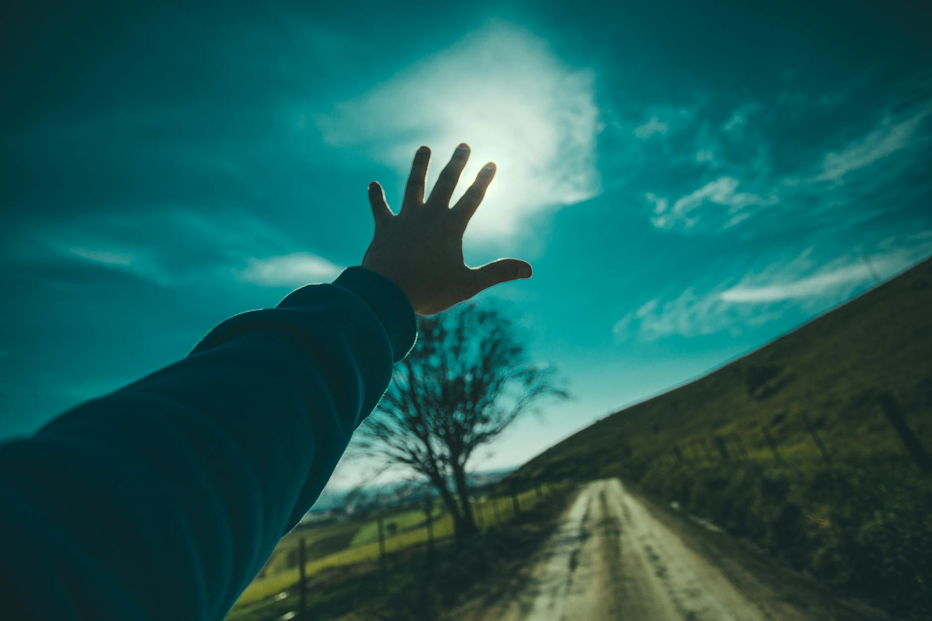 person raising hand towards blue sky during daytime