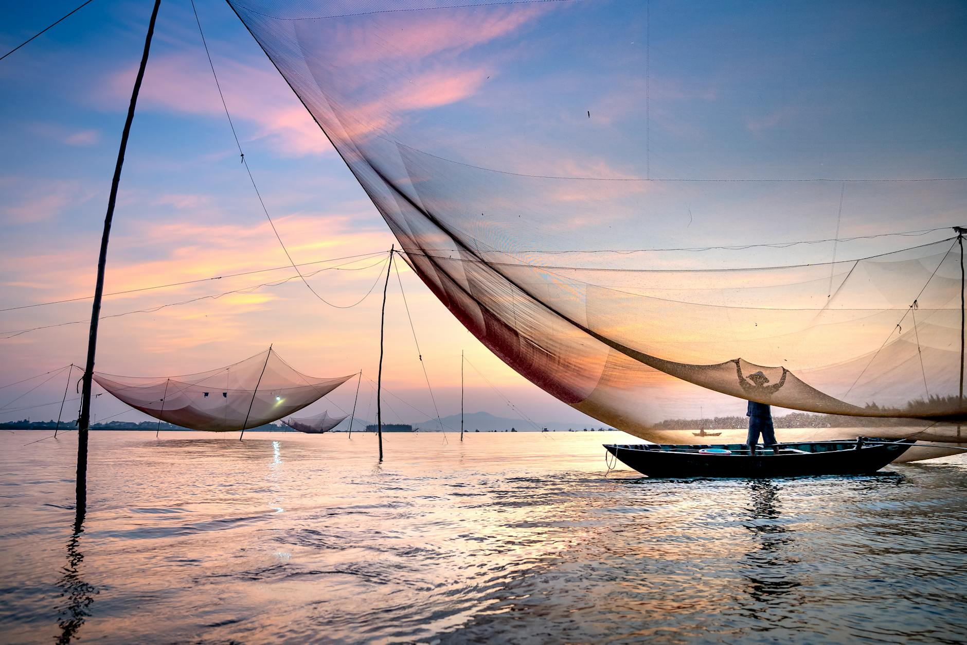 unrecognizable man catching fish with large net standing in boat moored on river